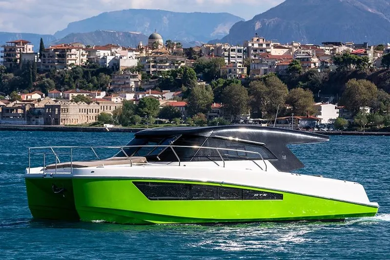  Yacht Photos Pics 2025 Makai M37 catamaran with vibrant green hull, cruising near scenic coastal town.