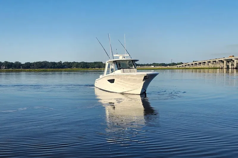  Yacht Photos Pics 2023 Pursuit S 378 Sport boat cruising on calm water near a bridge.