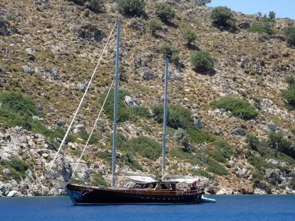 Trİppİn Yacht Photos Pics Wooden Ketch Tirhandil 20M, 2006, anchored near rocky hillside, clear blue water.
