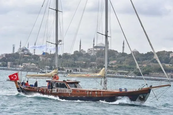 Trİppİn Yacht Photos Pics Wooden Ketch Tirhandil 20M sailing near historic cityscape, 2006 model, Turkish flag visible.