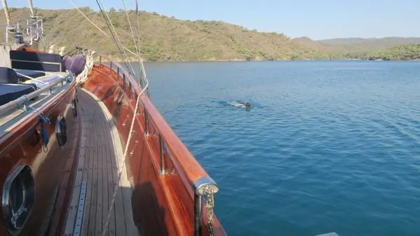 Trİppİn Yacht Photos Pics Wooden Ketch Tirhandil 20M sailing in serene waters near a hilly coastline, 2006 model.