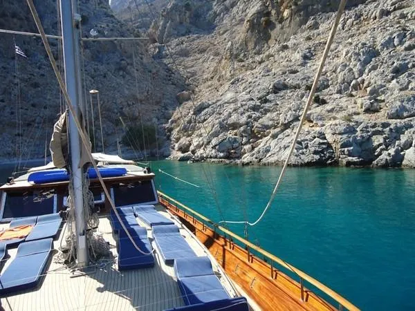 Trİppİn Yacht Photos Pics Wooden Ketch Tirhandil 20M sailing in clear turquoise waters near rocky cliffs, 2006 model.