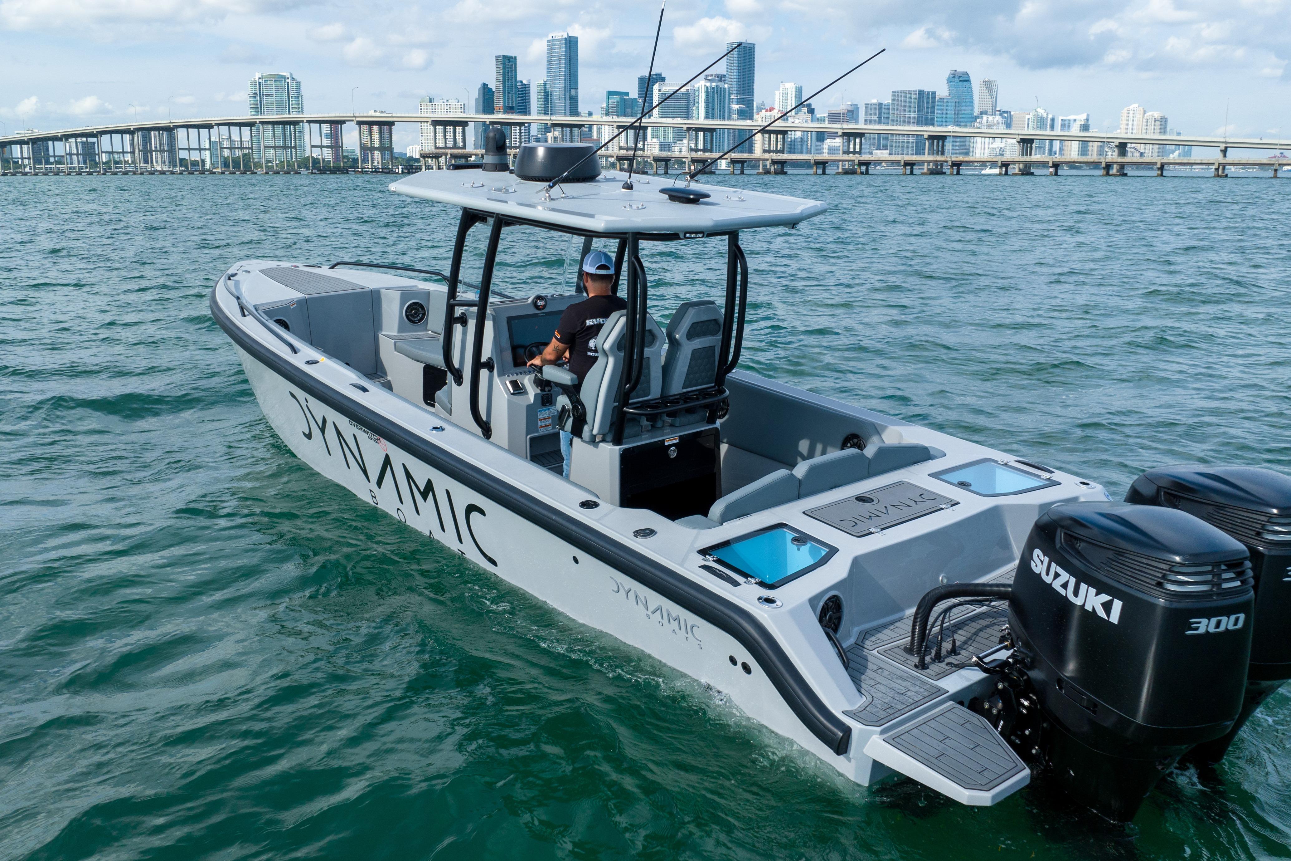 Dynamic D-305V boat cruising with city skyline in background, featuring dual Suzuki engines.