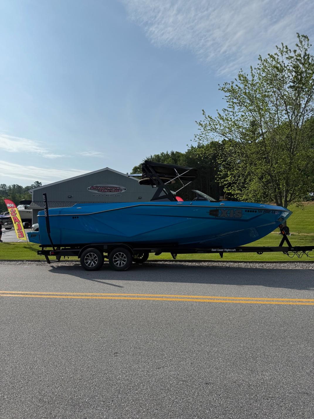 Blue 2022 Axis T250 boat on trailer, parked near a building and trees.