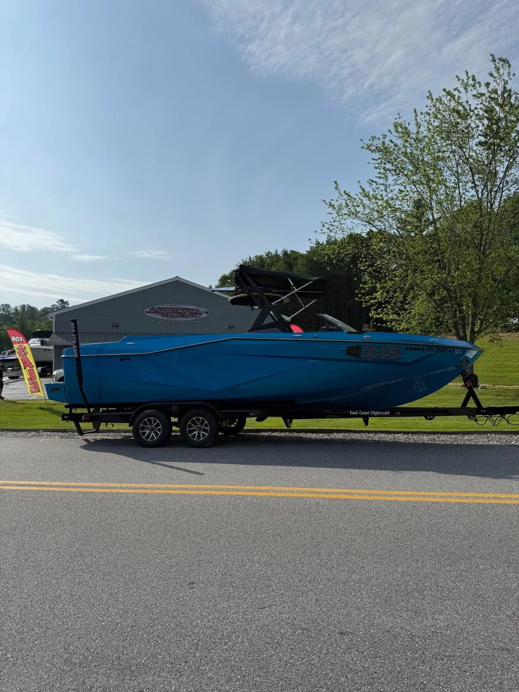 Blue 2022 Axis T250 boat on trailer, parked near a building and trees.