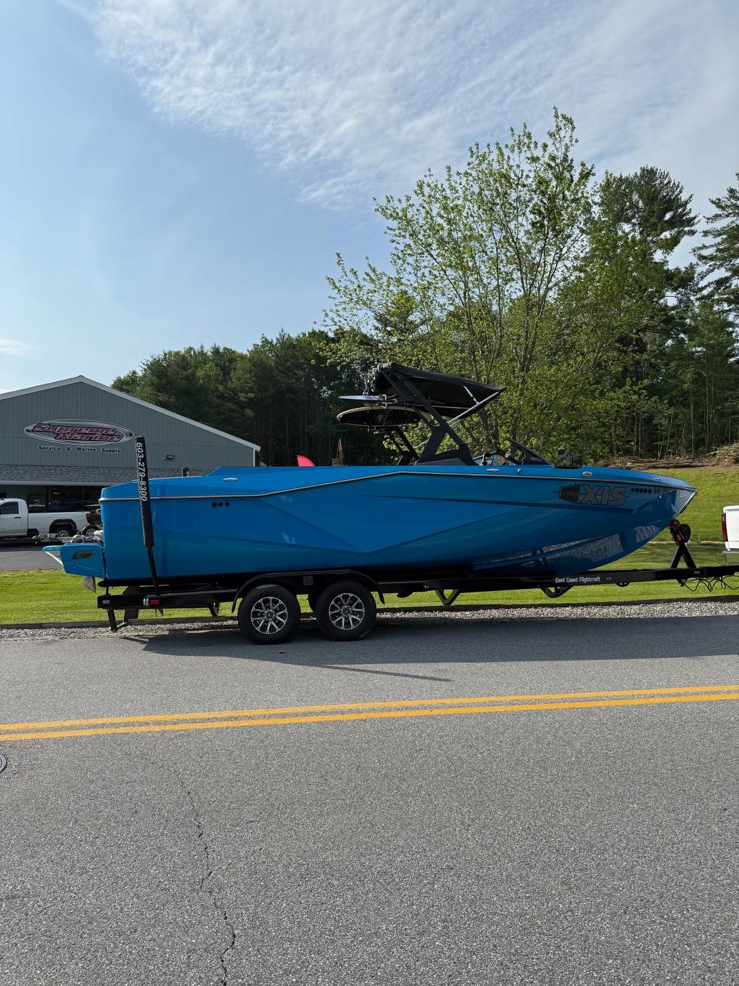 Blue 2022 Axis T250 boat on trailer, parked near a building and trees.