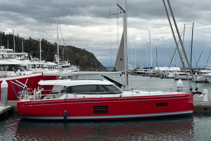 In Stock - W / Warranty Yacht Photos Pics Red 2024 Moody 41ds sailboat docked in a marina under cloudy skies.