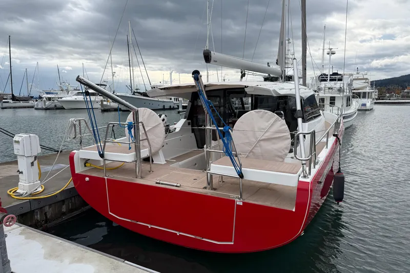 In Stock - W / Warranty Yacht Photos Pics 2024 Moody 41ds sailboat with red hull docked at marina under cloudy sky.