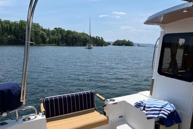 Mystic Yacht Photos Pics 2014 Ranger Tugs R-31 on serene lake with forested shoreline and sailboat in distance.