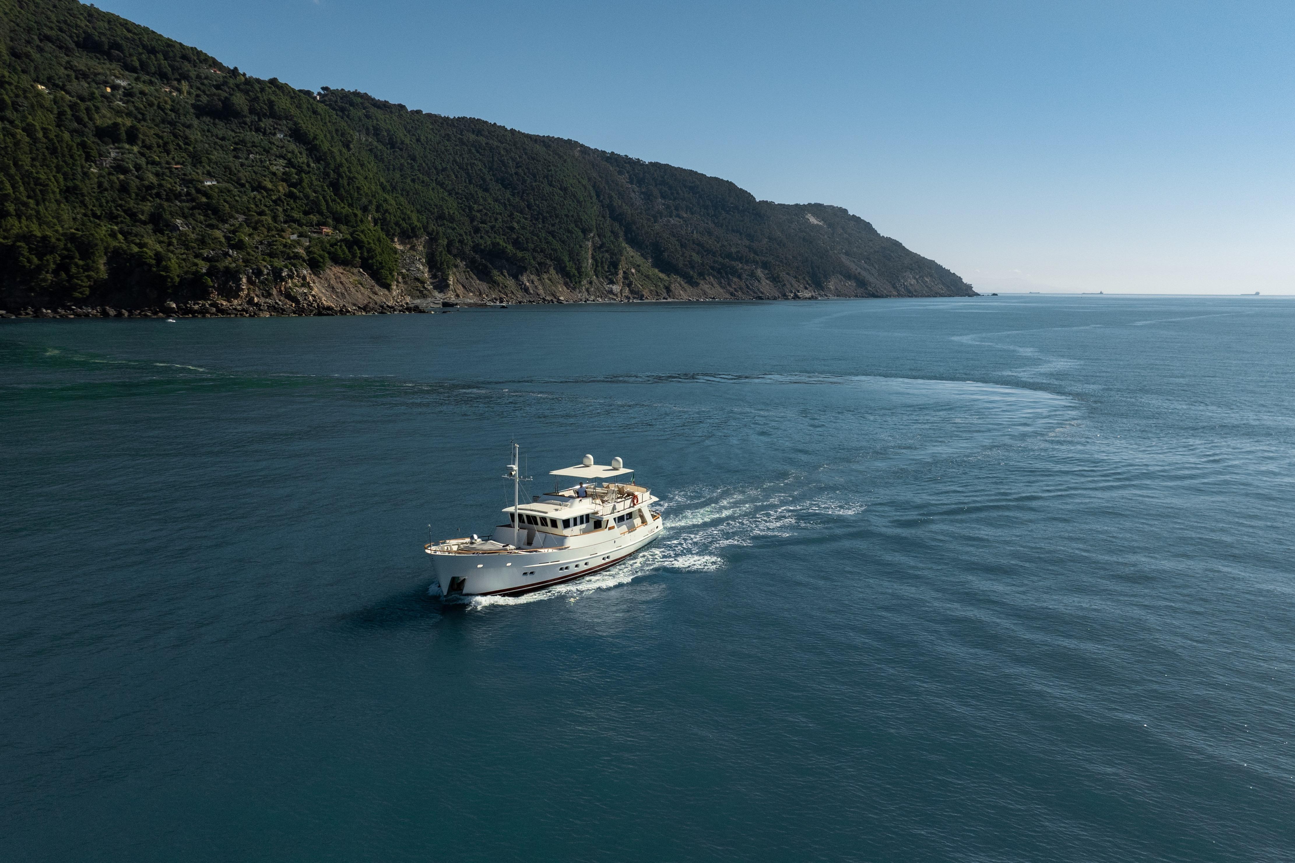 2000 Bugari NAVETTA yacht cruising near a lush, mountainous coastline.