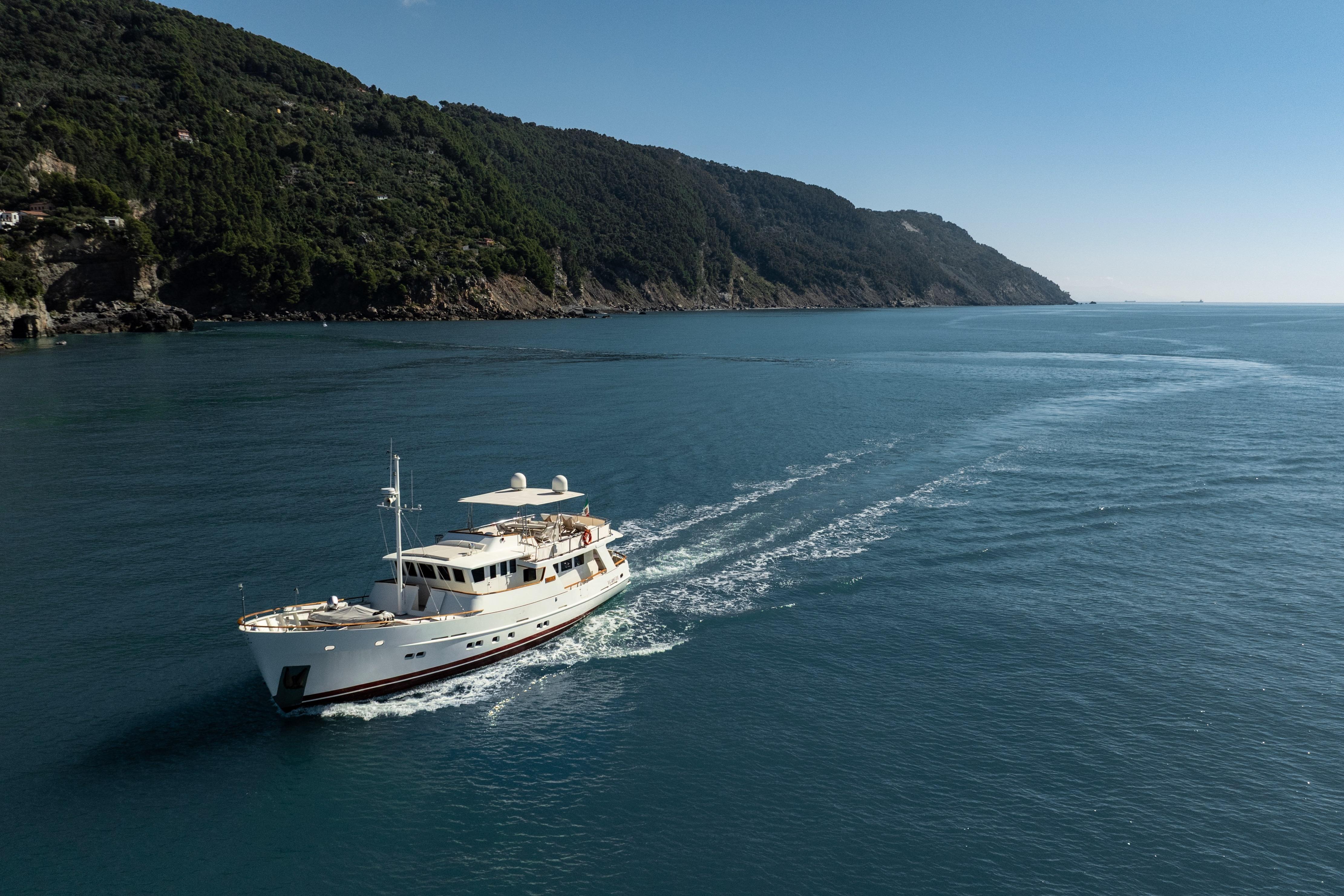 2000 Bugari NAVETTA yacht cruising along scenic coastline under clear blue sky.