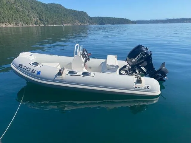 Yacht Photos Pics White inflatable boat with outboard motor on calm water, surrounded by forested hills.