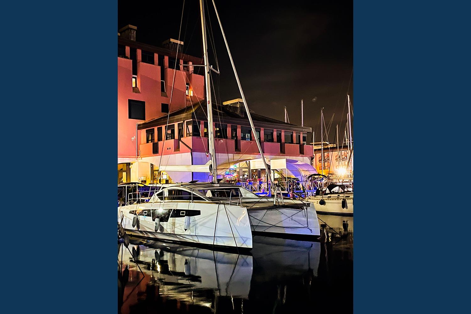 Sailboat Comar C-CAT 37, 2021 model, docked at night near illuminated building.