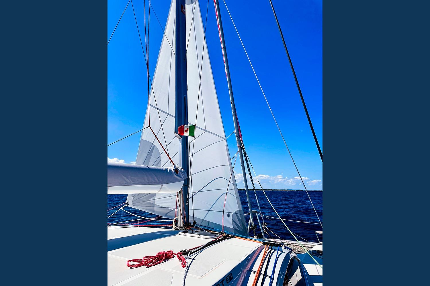 Sailing on a 2021 Comar C-CAT 37 catamaran with white sails against a clear blue sky.