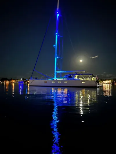 Serenity Yacht Photos Pics 2016 Jeanneau 64 sailboat illuminated at night, reflecting on calm water.