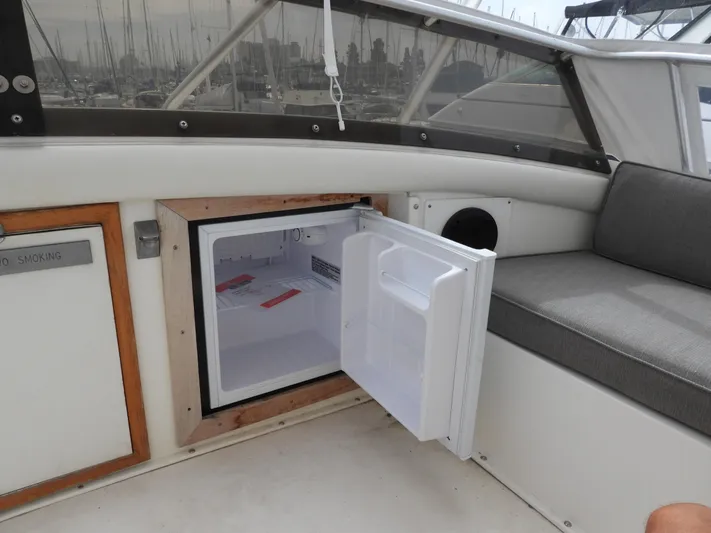  Yacht Photos Pics 1989 Bertram Convertible boat interior with open mini fridge and cushioned seating.