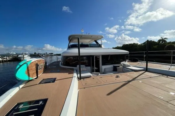 Sunlove Yacht Photos Pics 2024 Lagoon SIXTY 7 yacht with spacious deck and paddleboard, docked under clear skies.