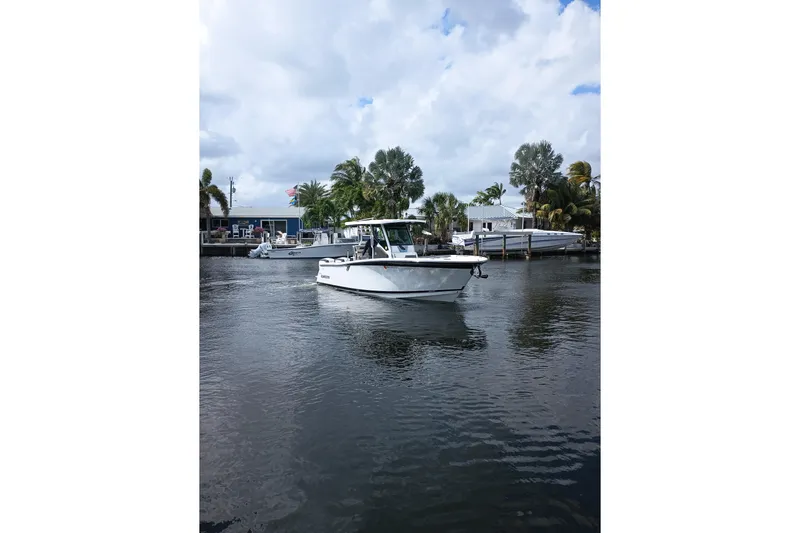  Yacht Photos Pics 2020 Blackfin 272 CC boat on a calm waterway, surrounded by palm trees and houses.