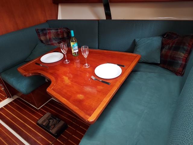 Cozy dining area in 1986 Pearson 36-2 sailboat with wooden table and teal seating.