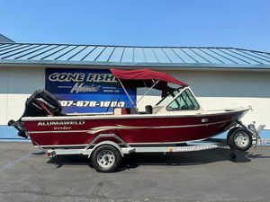 2003 Alumaweld Stryker boat with red canopy on trailer, parked outside marine shop.