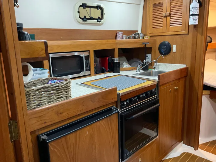  Yacht Photos Pics 2000 Mainship Pilot boat kitchen with wooden cabinetry, stove, microwave, and sink.