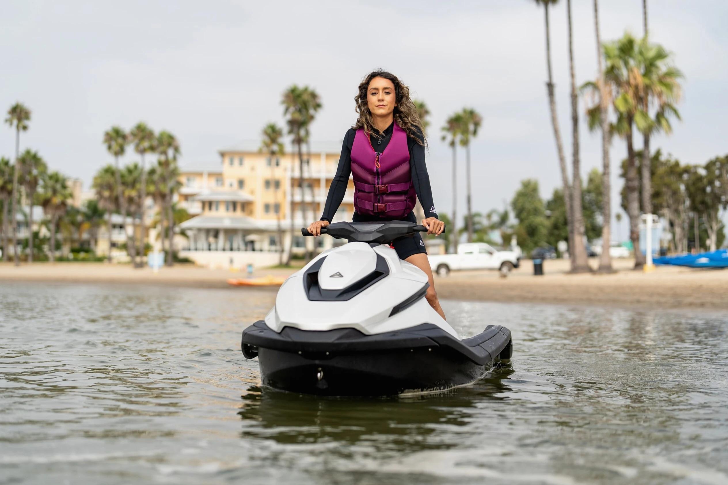 Woman riding 2025 Taiga Orca P2 jet ski near a beach with palm trees.
