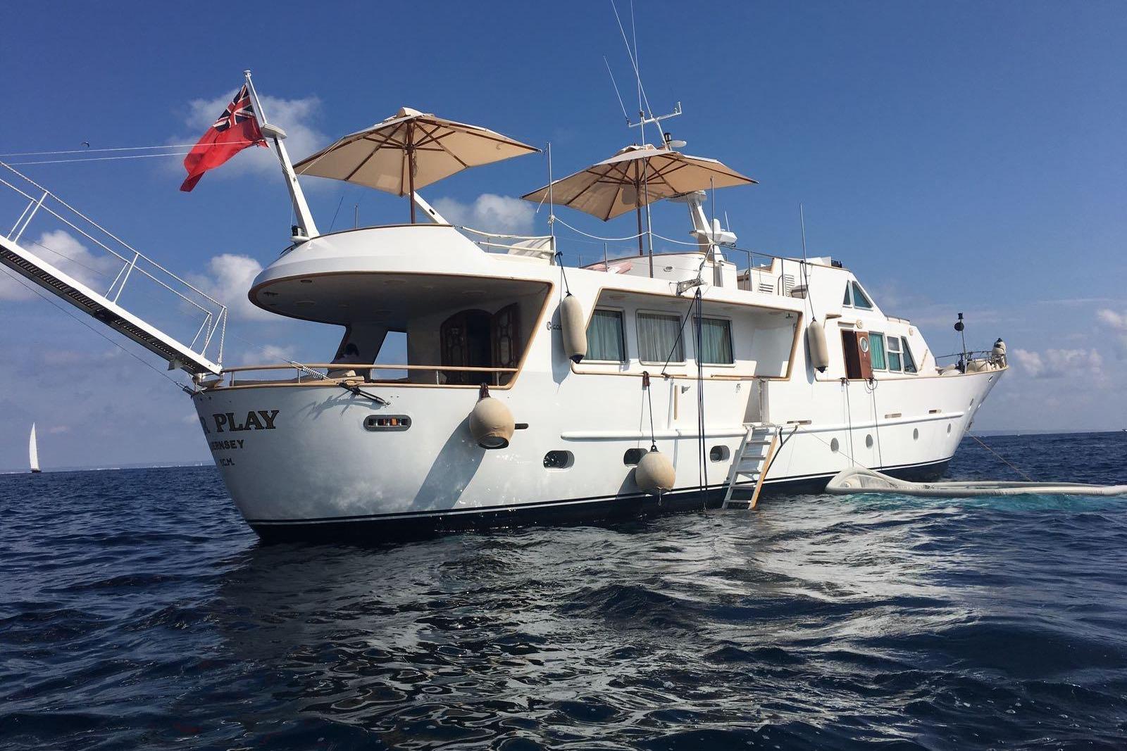 Luxurious 1977 Codecasa 27m yacht with umbrellas, anchored in calm sea under clear blue sky.