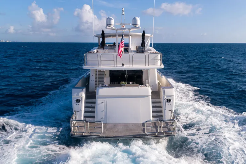 Aleniel Yacht Photos Pics Johnson 87' Motor Yacht 2005 cruising on open sea, rear view with American flag.