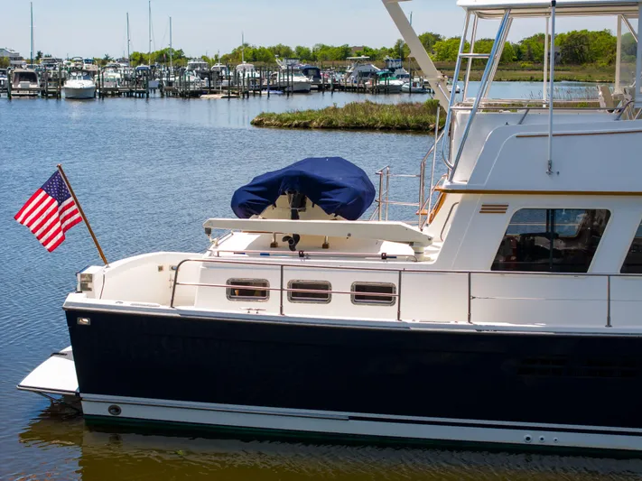 Nellie Yacht Photos Pics 1998 Sabreline 47 Aft Cabin Trawler docked, featuring American flag and scenic marina backdrop.