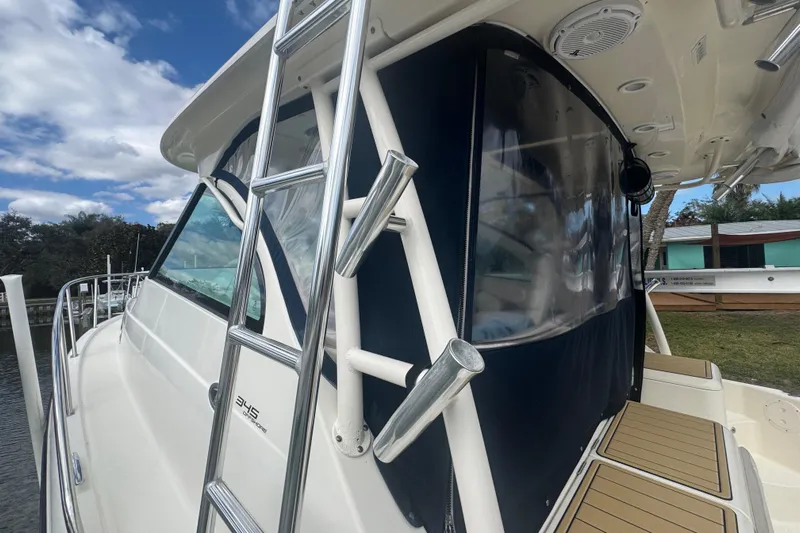  Yacht Photos Pics 2014 Pursuit OS 345 Offshore boat with ladder and enclosed cabin, docked under a cloudy sky.