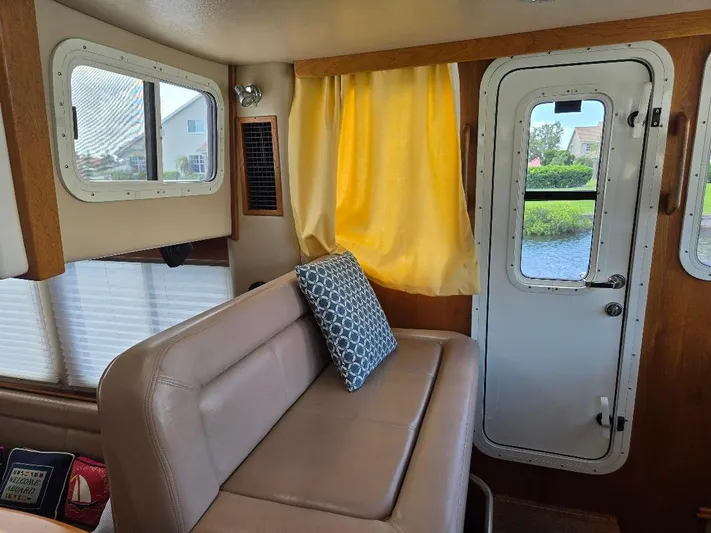Ecola Yacht Photos Pics Interior of 2005 American Tug 34 Pilothouse with beige seating, yellow curtains, and a scenic window view.