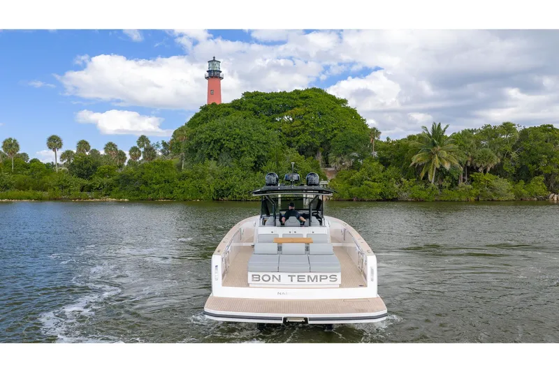  Yacht Photos Pics 2024 Pardo Yachts 43 cruising near lush greenery and a lighthouse under a partly cloudy sky.