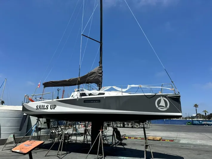 Sails Up Yacht Photos Pics 2022 Beneteau First 27 sailboat on stands, labeled "Sails Up," under clear blue sky.