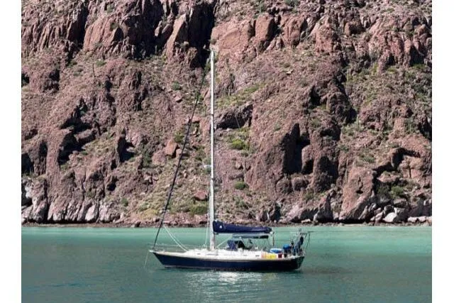 Unicorn Yacht Photos Pics Sailboat Hylas Custom 44 (1988) anchored near rocky cliffs in turquoise water.