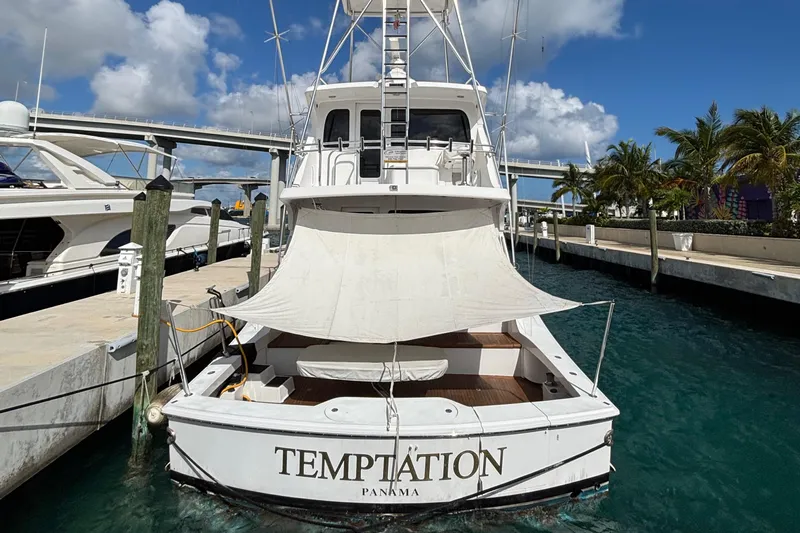 Temptation Yacht Photos Pics 2008 Hatteras 77 Convertible yacht docked, named "Temptation," with a sunshade, in a marina.