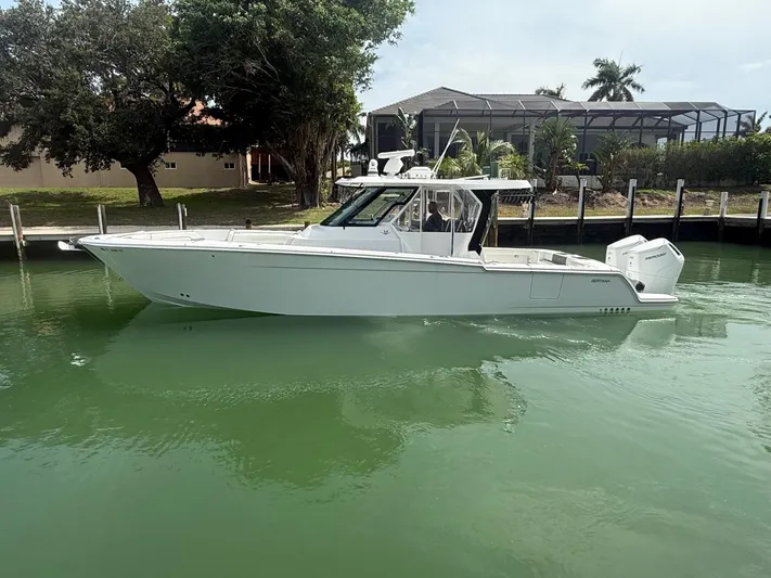  Yacht Photos Pics 2023 Bertram 39 CC boat docked in calm waters, surrounded by lush greenery.