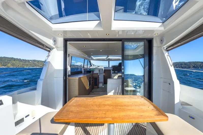 Bee's Knees Yacht Photos Pics 2017 Jeanneau NC 14 yacht interior with wooden table, panoramic windows, and ocean view.