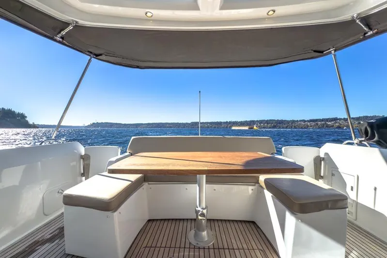 Bee's Knees Yacht Photos Pics 2017 Jeanneau NC 14 yacht deck with seating and table, overlooking serene water.