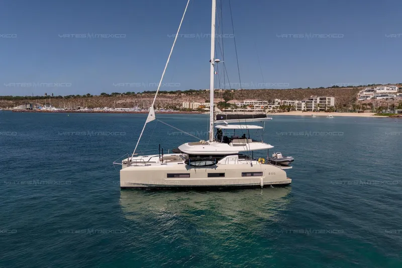  Yacht Photos Pics 2023 Lagoon 55 yacht anchored in serene coastal waters, with scenic shoreline backdrop.