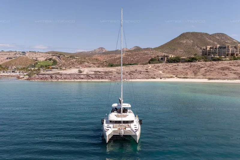  Yacht Photos Pics 2023 Lagoon 55 catamaran anchored in clear blue waters near a scenic coastline.