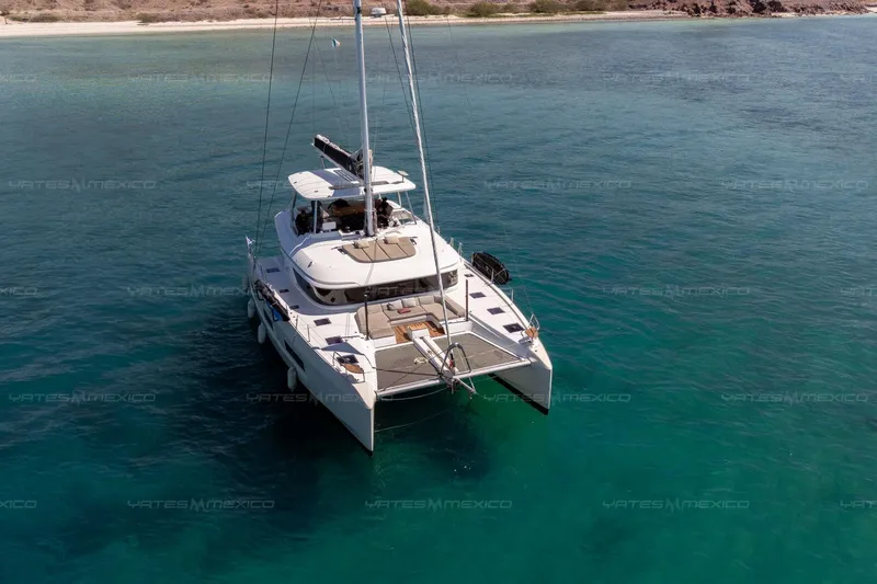  Yacht Photos Pics 2023 Lagoon 55 catamaran sailing in clear turquoise waters near a sandy shoreline.
