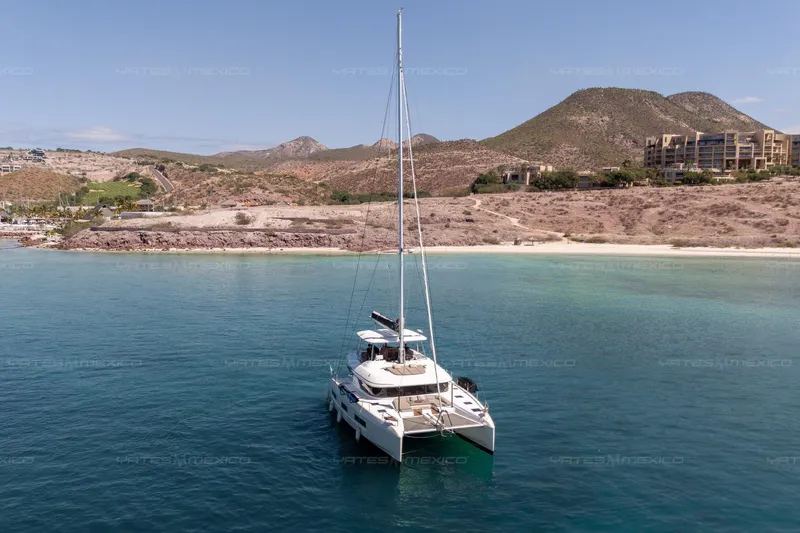  Yacht Photos Pics 2023 Lagoon 55 catamaran anchored in clear blue waters near a rocky coastline.