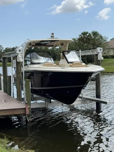  Yacht Photos Pics 2023 Scout 277 Dorado boat on lift by waterfront dock, under partly cloudy sky.