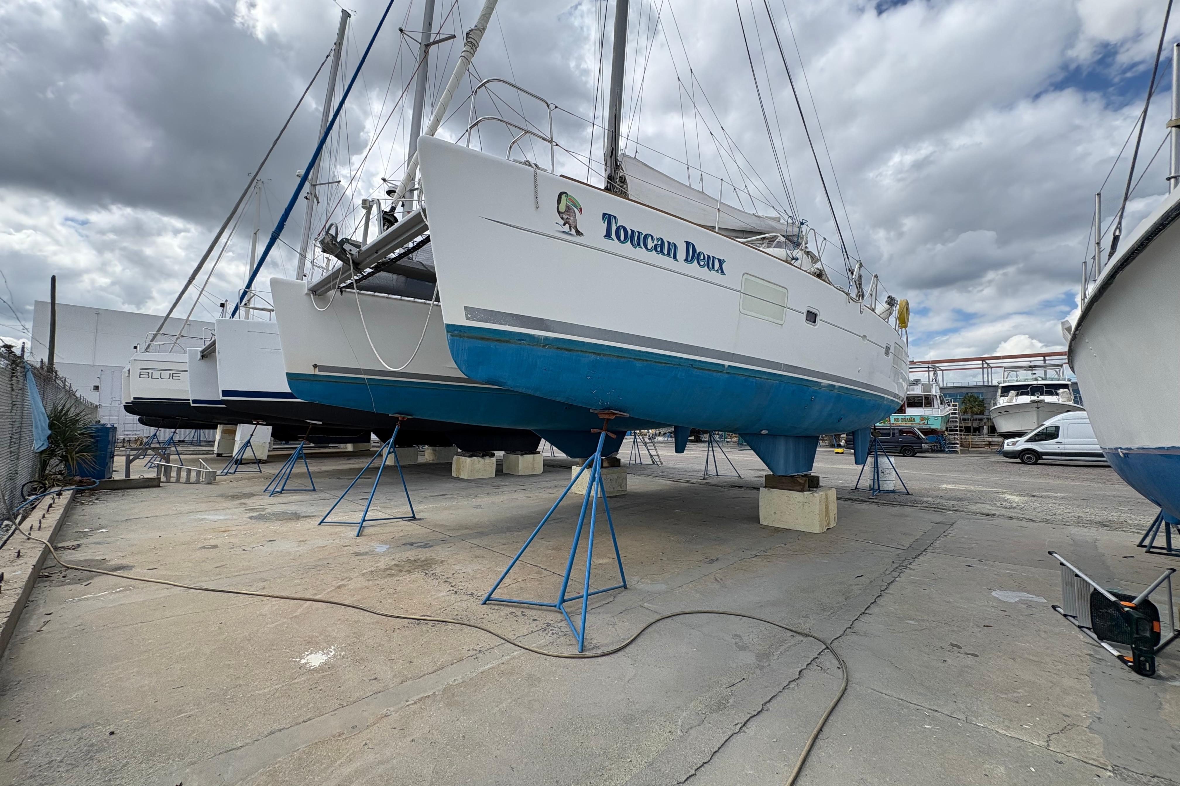 2004 Lagoon 380 catamaran "Toucan Deux" on dry dock under cloudy sky.