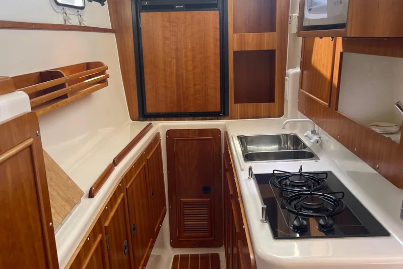 Two Buoys Yacht Photos Pics Interior of 2002 PDQ 32 Power Catamaran kitchen with stove, sink, and wooden cabinetry.