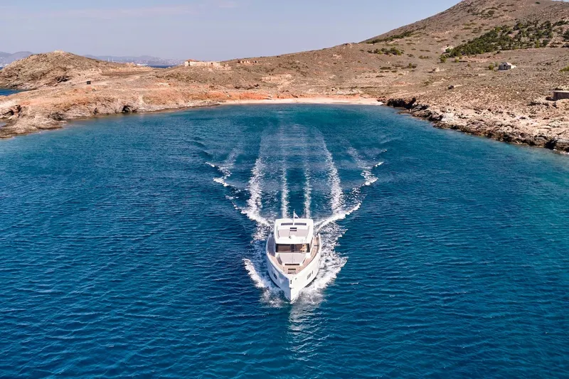  Yacht Photos Pics 2026 Omikron Yachts OT-60 cruising in clear blue waters near rocky coastline.