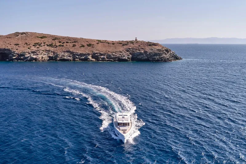  Yacht Photos Pics 2026 Omikron Yachts OT-60 cruising near rocky coastline under clear blue sky.