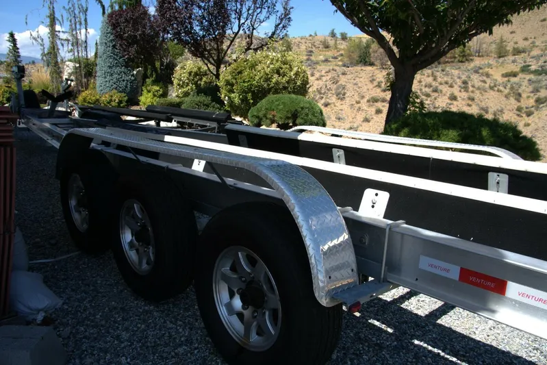  Yacht Photos Pics Triple-axle boat trailer parked on gravel, surrounded by lush greenery and hills.
