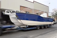 2025 Olbap TR12 Open boat on trailer, blue and white design, parked near industrial building.