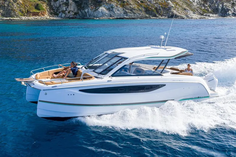  Yacht Photos Pics Manufacturer Provided Image: 2026 Jeanneau TH38 cruising on clear blue waters near rocky coastline.